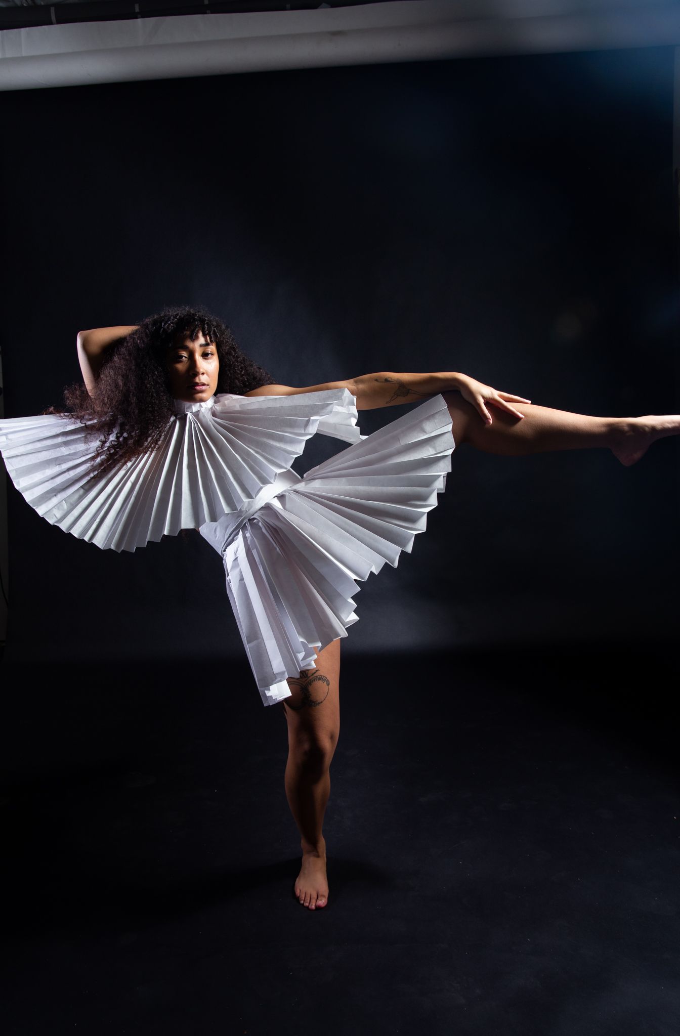 Woman in white pleated dress balances in a dance pose against a dark background; art by Matt Remsbecher. 