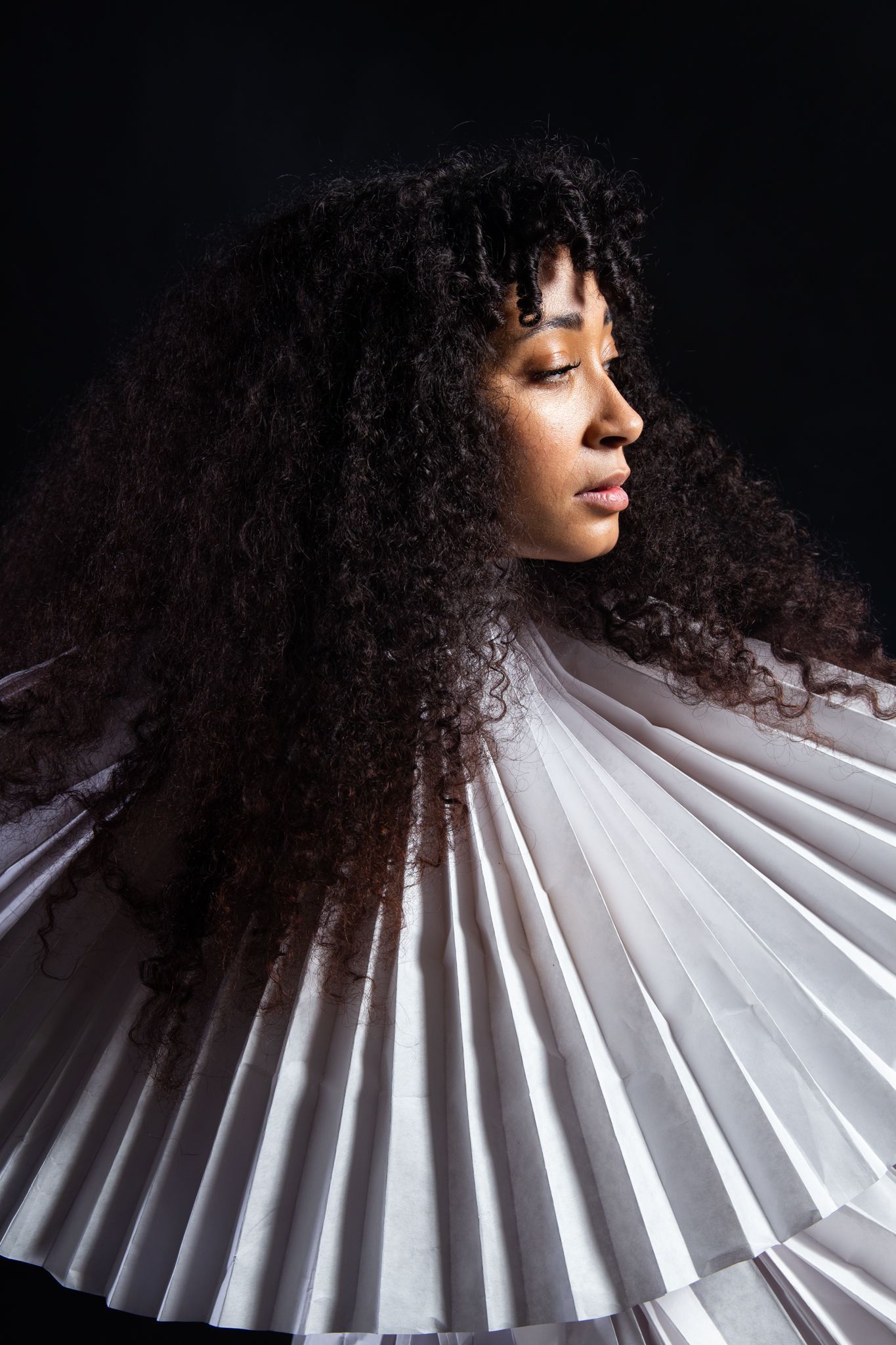 Woman with curly hair in a white, pleated collar, looking right, dark background; art by Matt Remsbecher. 