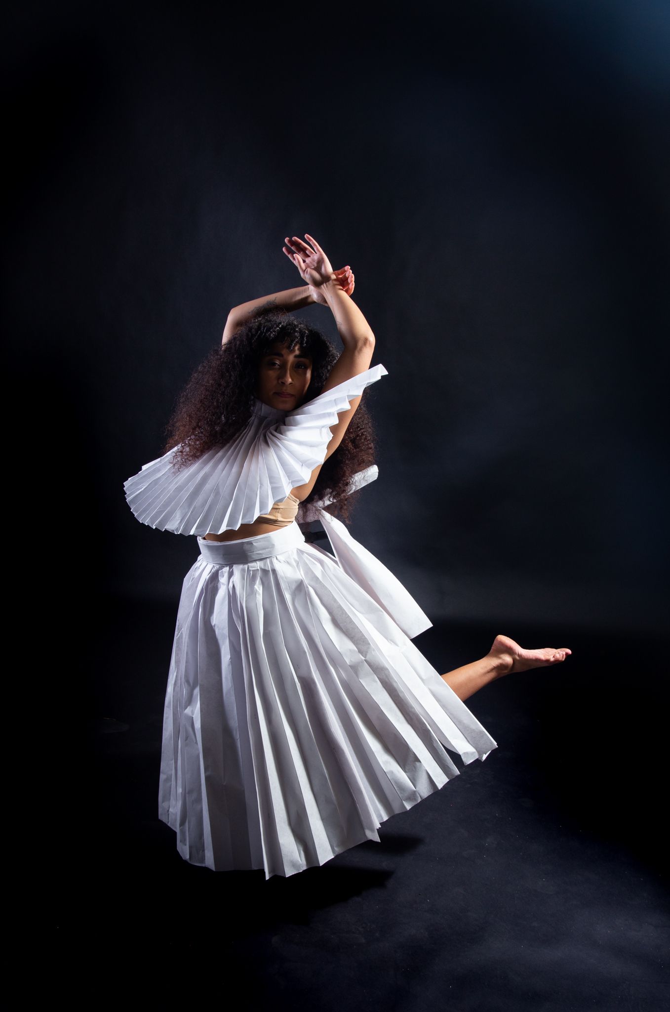 Dancer in white pleated skirt and ruffle-collared top, in mid-air pose against dark background; art by Matt Remsbecher. 