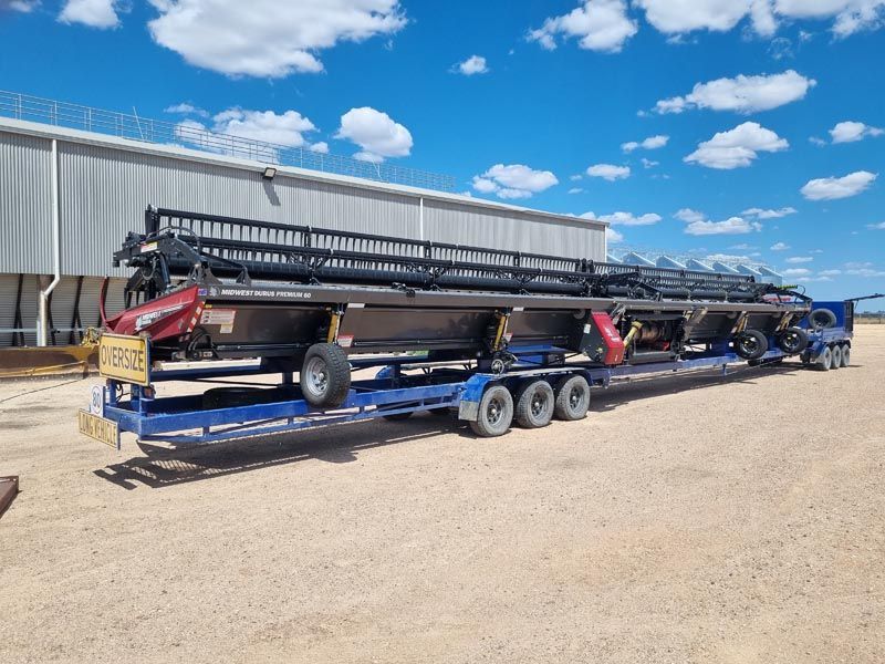 A truck is carrying a very long trailer with a combine harvester on it.