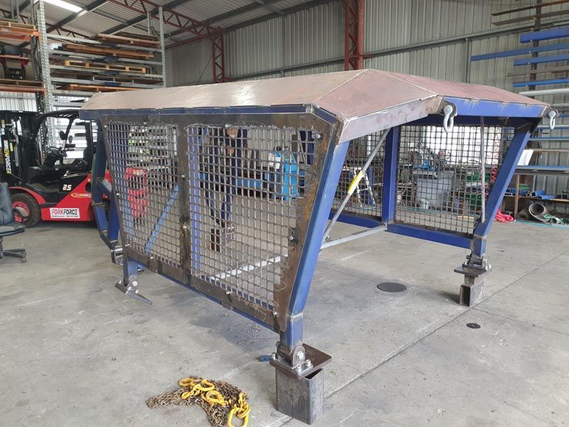 A metal structure is sitting in a warehouse next to a forklift.