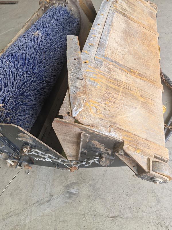 A close up of a broom with blue bristles on a concrete surface.