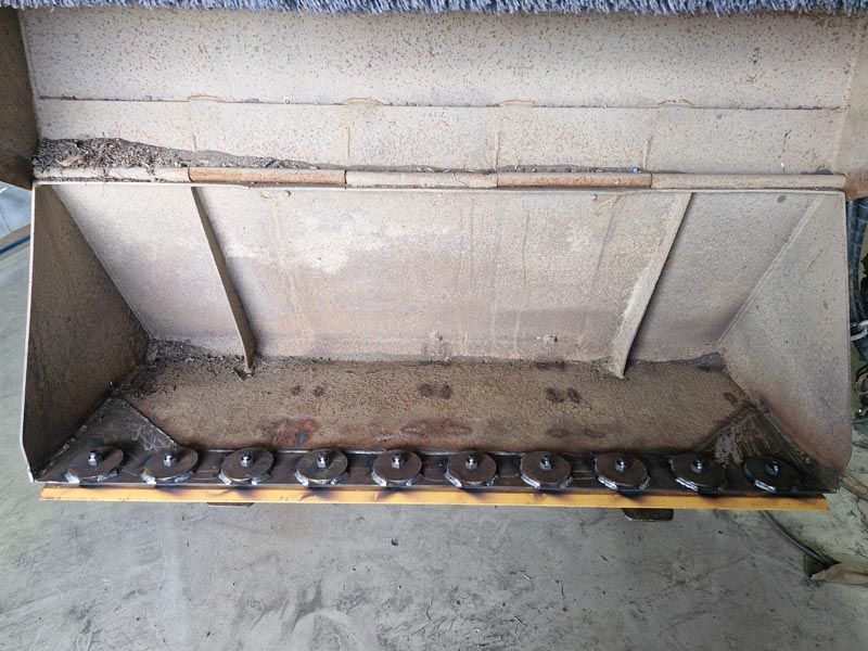 A metal bucket with chains on it is sitting on the ground