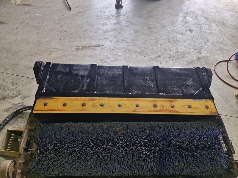 A black and yellow brush is sitting on a concrete floor.