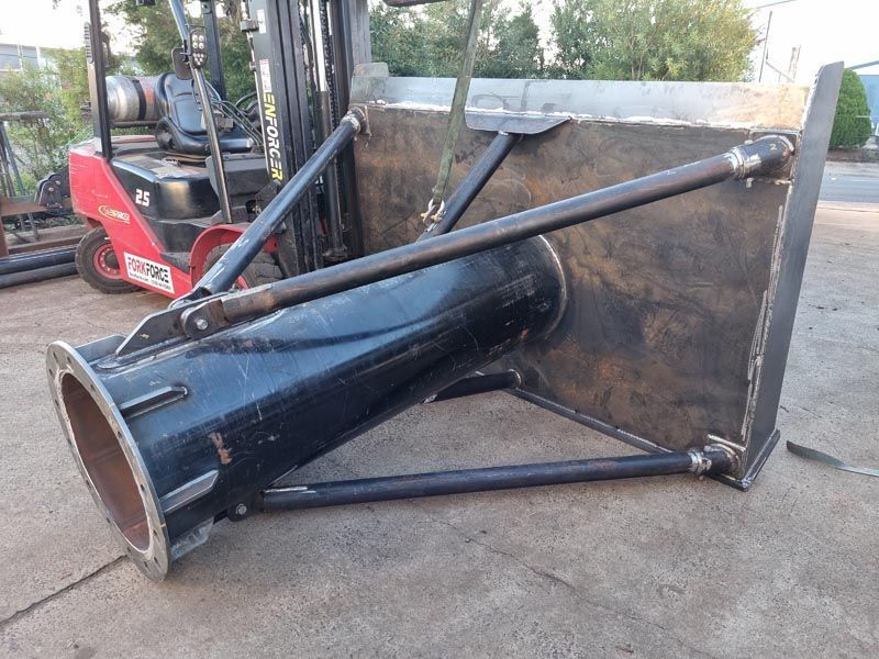 A large piece of metal is sitting on the ground next to a forklift.