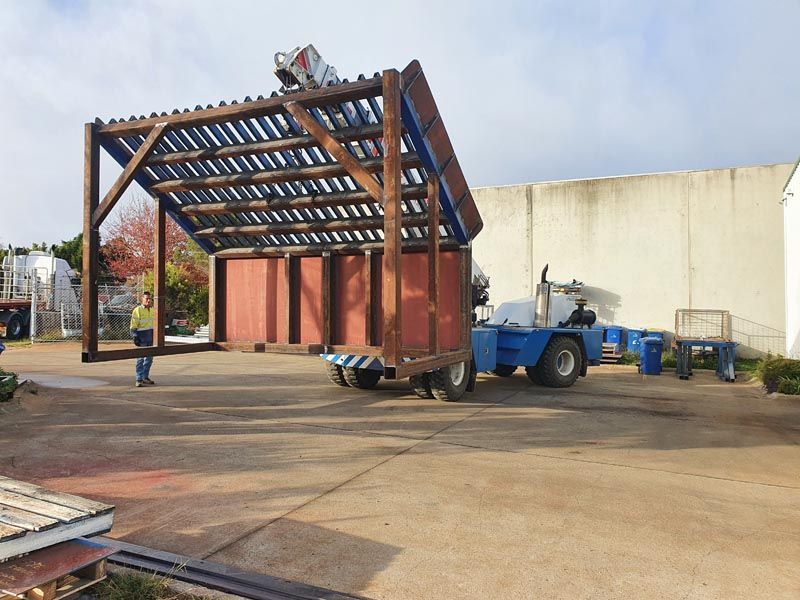 A large wooden structure is being lifted by a forklift in a parking lot.