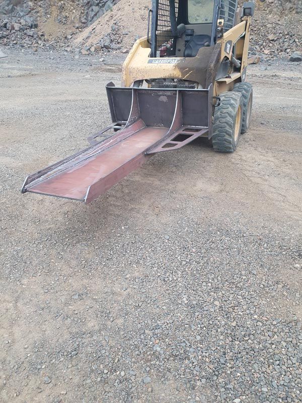 A bulldozer with a ramp attached to it is parked on a gravel road.