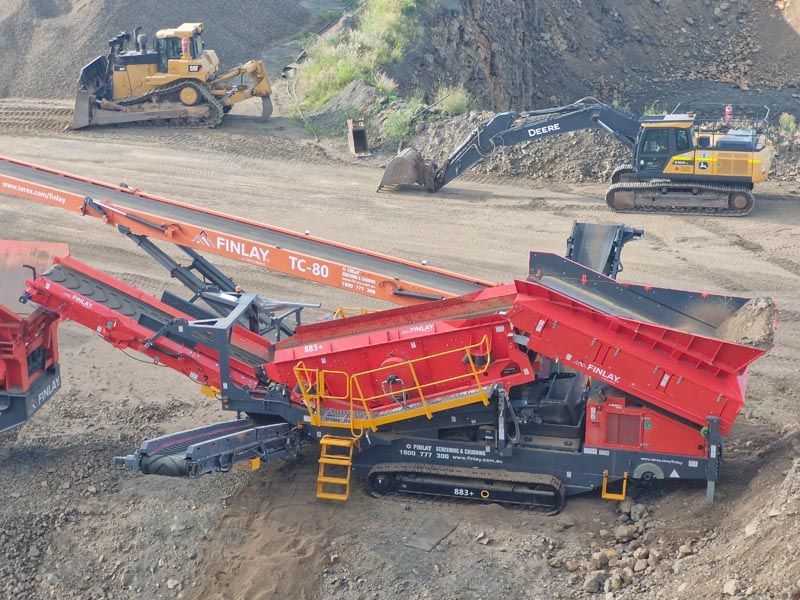 A red and black machine is sitting in the dirt in a quarry.