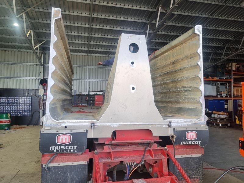 A dump truck is parked in a warehouse with the word muscat on the side.