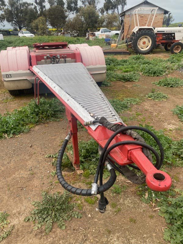 A red trailer is parked in a field next to a tractor.