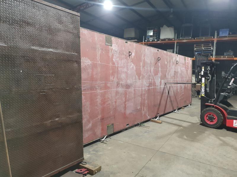A forklift is moving a large piece of metal in a warehouse.