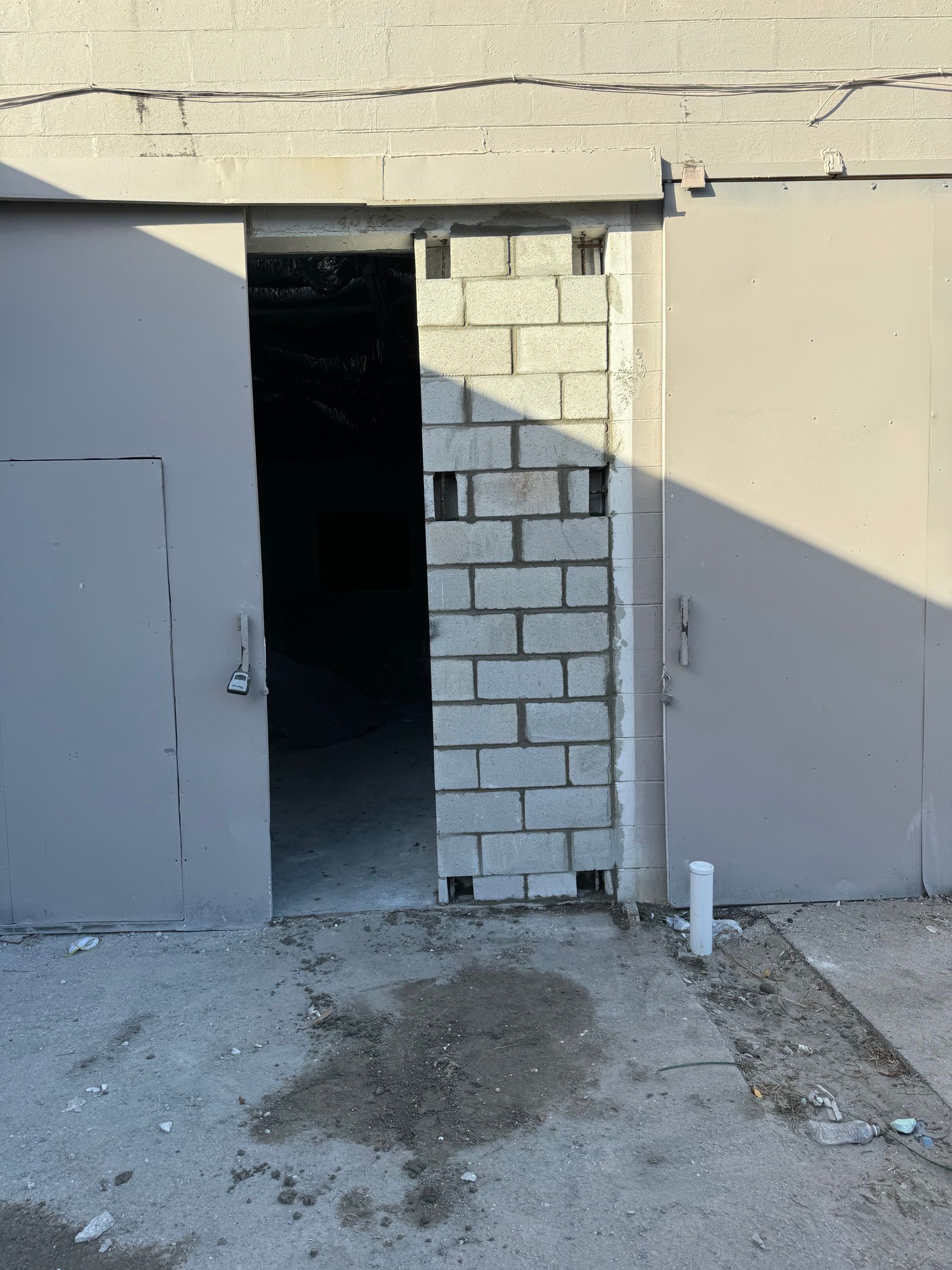 Gray cinder block wall between two gray metal garage doors; concrete ground.