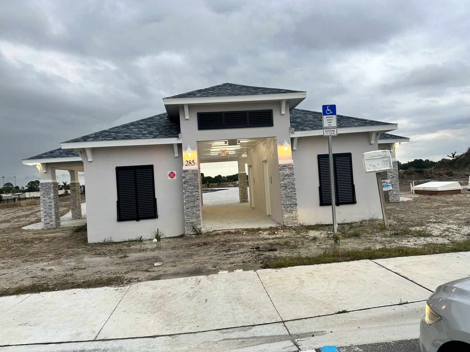 A light-colored restroom building under a cloudy sky. Includes handicap parking sign.
