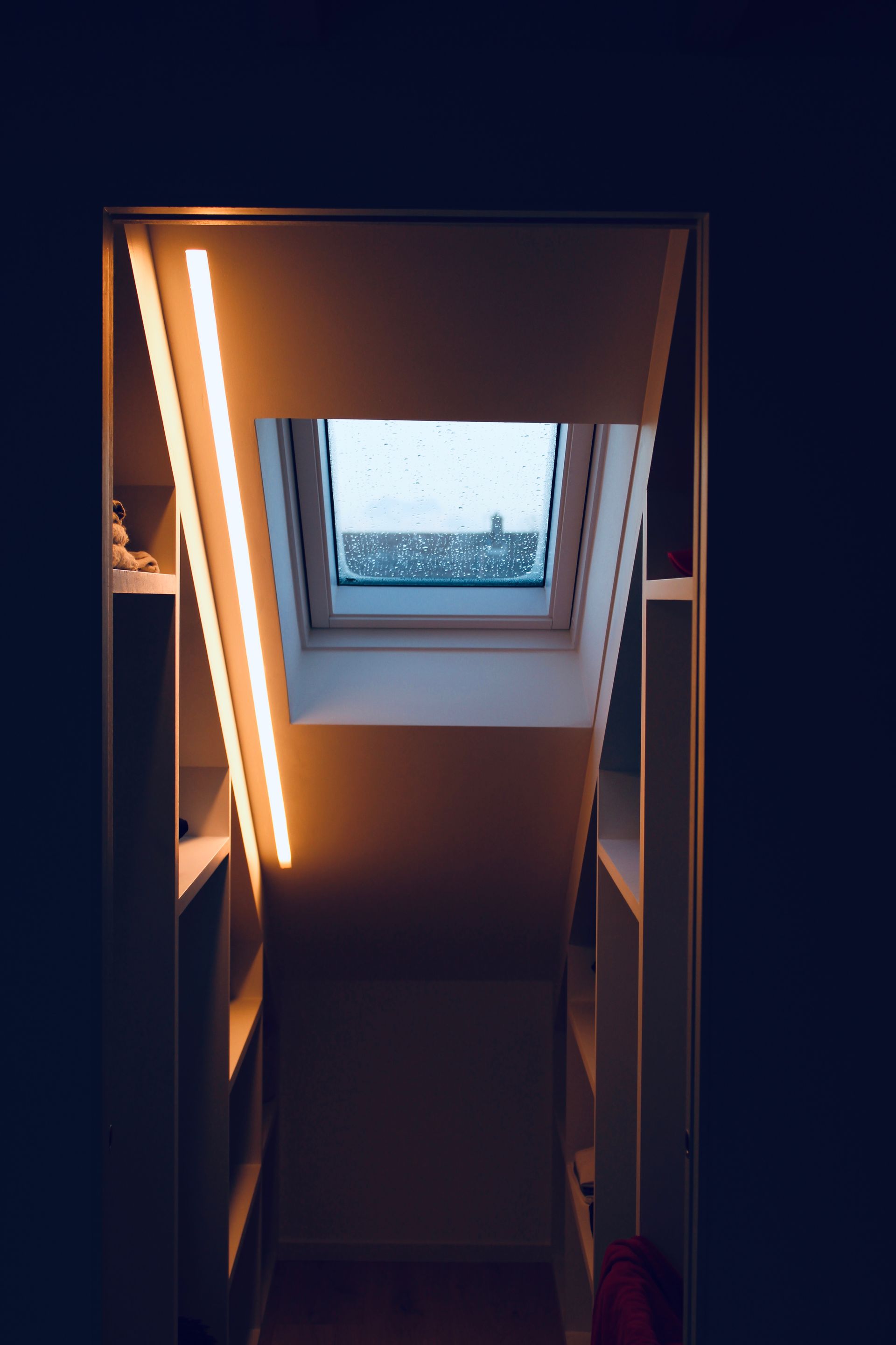 Staircase with skylight; built-in shelves on both sides with warm, linear lighting.