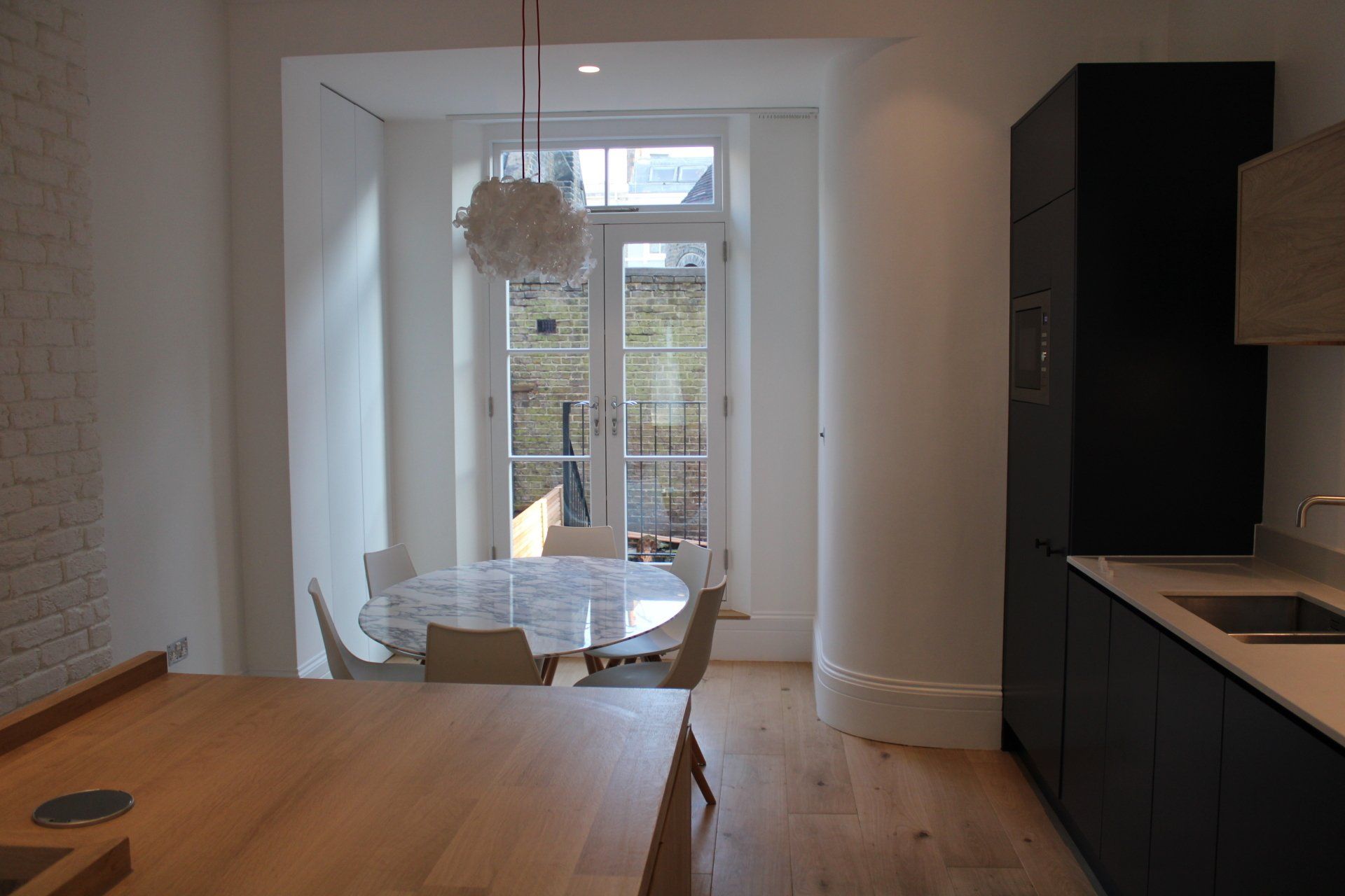 Modern kitchen with a round table near French doors. Black cabinets, wood floors, and white walls.