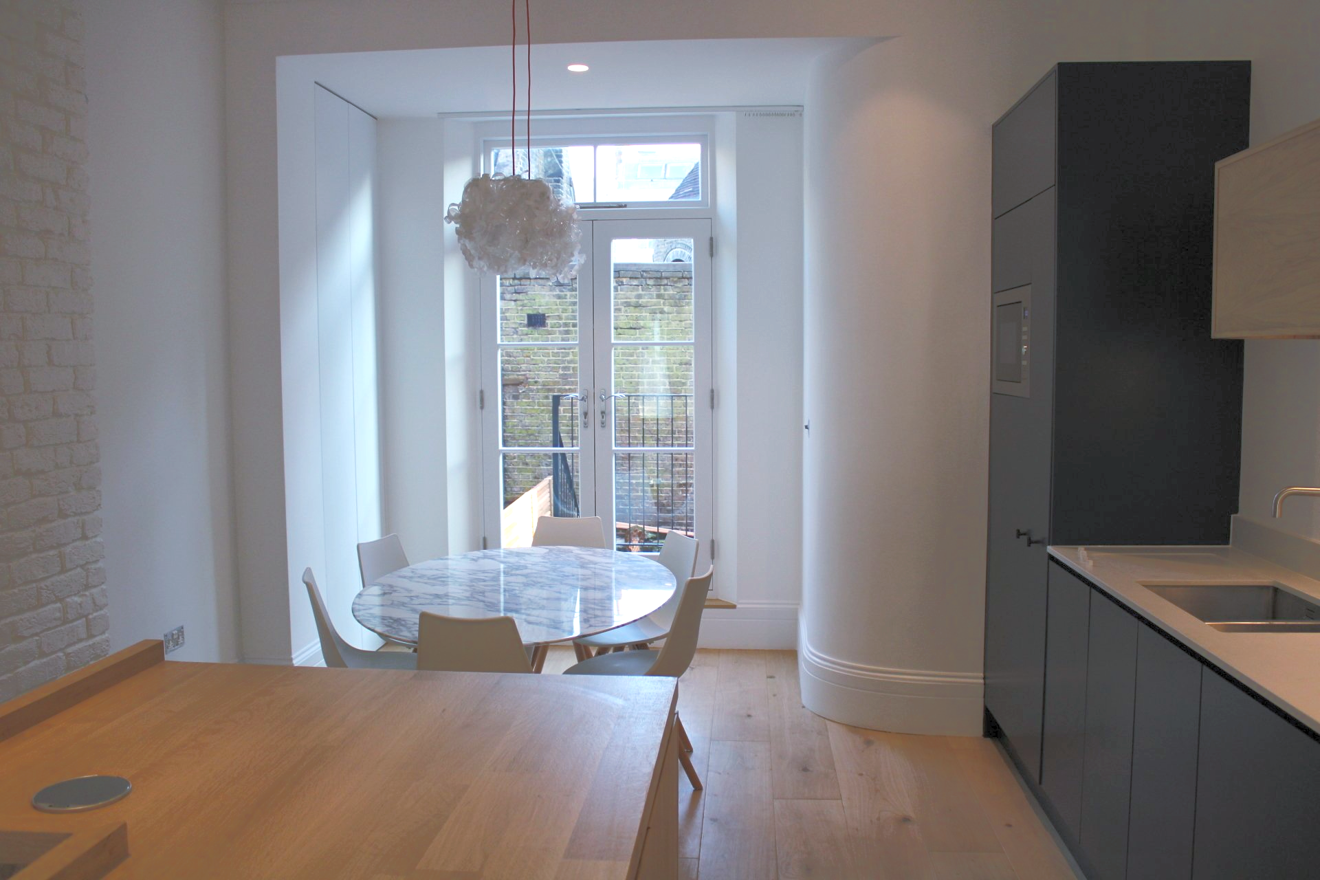Kitchen with table and chairs in front of French doors, dark gray cabinets, and light wood floor.