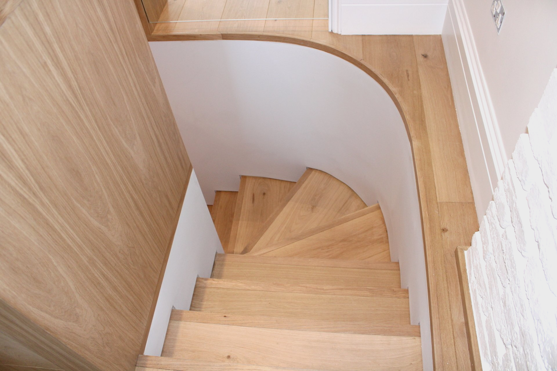 Wooden staircase curving downwards, with light oak treads, and white walls.