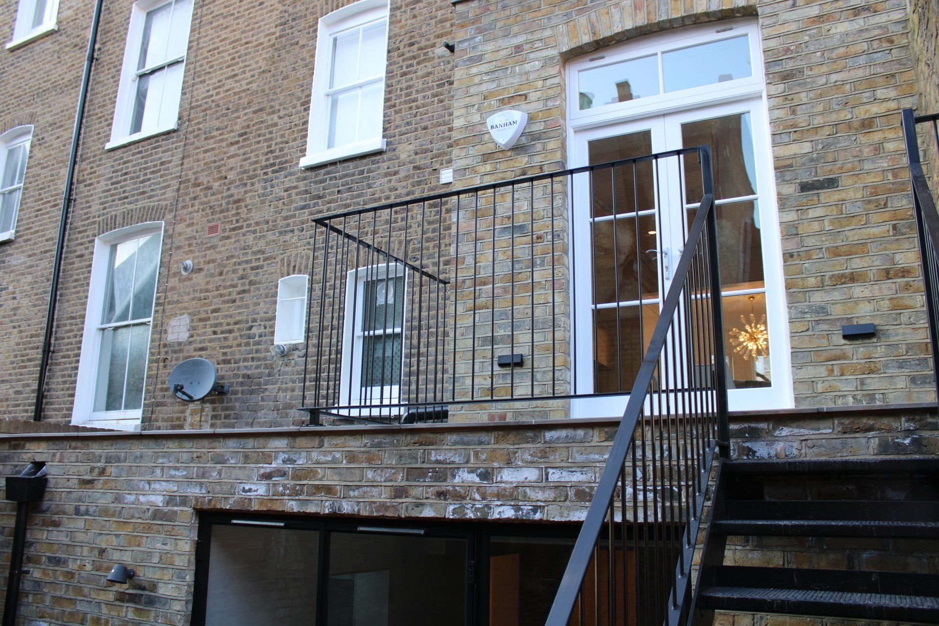 Exterior of a brick building with a balcony and metal staircase. French doors are open.