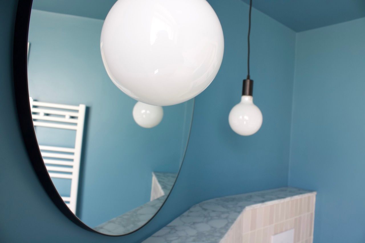Blue bathroom with round mirror, globe pendant lights.