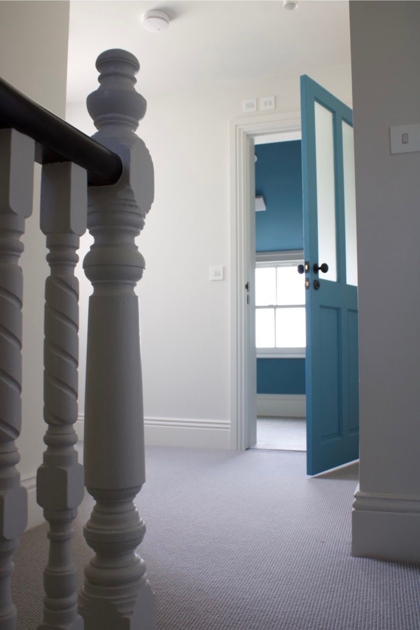 Hallway with a blue door ajar, showing a room with a window. The hallway has a stair railing.