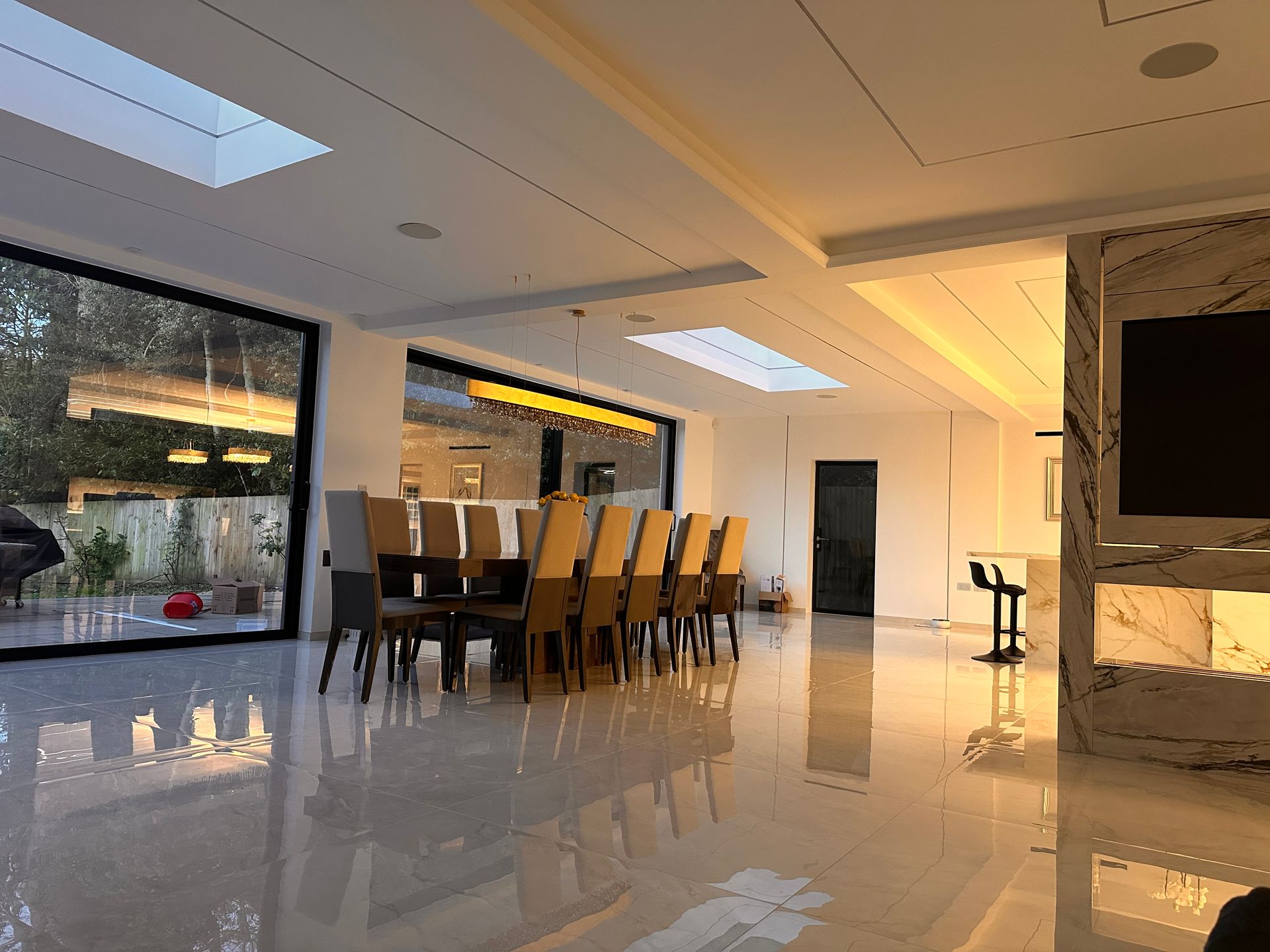 Spacious, modern dining room with long wooden table, large windows, and reflective, glossy floor.