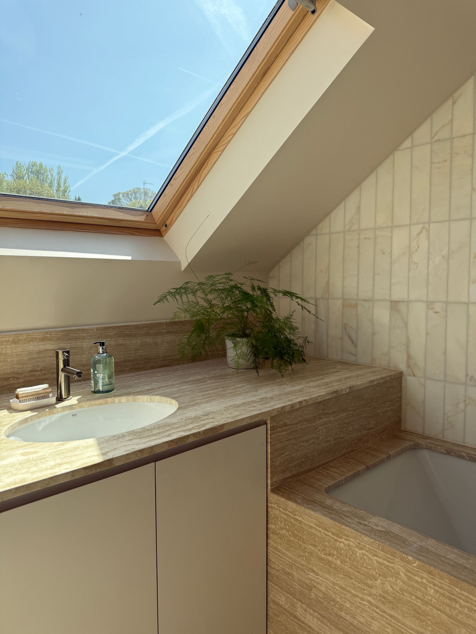 Bathroom with a skylight, a stone vanity with a sink, a bathtub, and tiled walls.