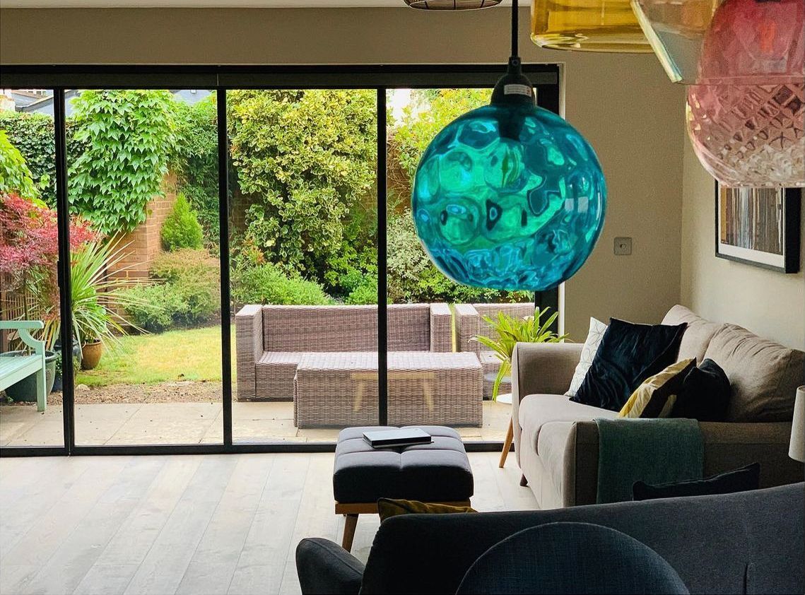 Living room with a glass door to a garden, turquoise glass light, and a sofa.