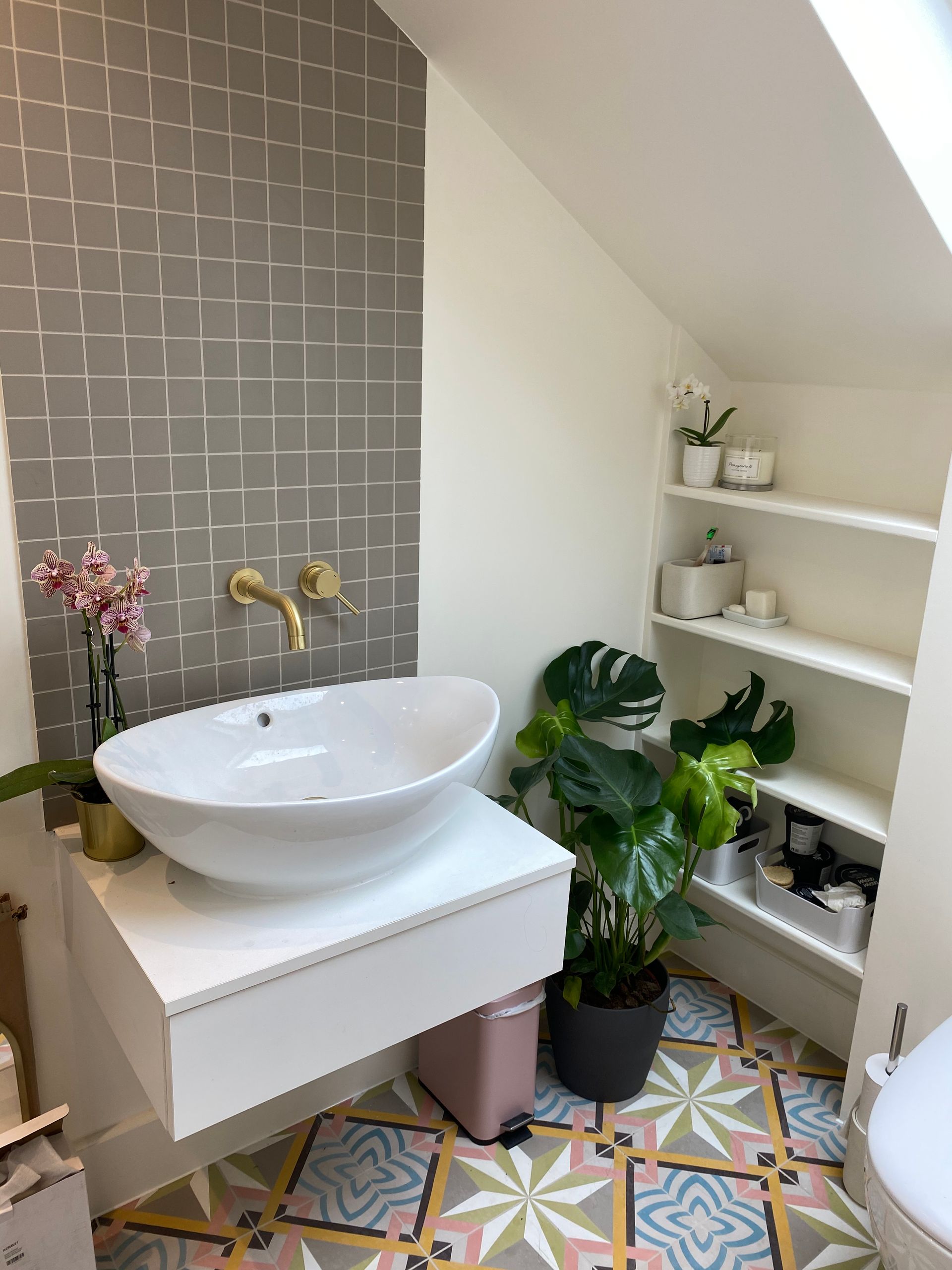 Bathroom with gray tiled accent wall, floating sink, shelves, patterned floor, and plants.