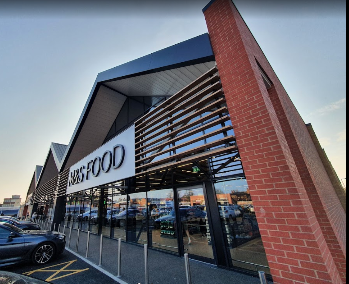 Exterior of M&S Food store with a modern design, red brick accents, and a car park.