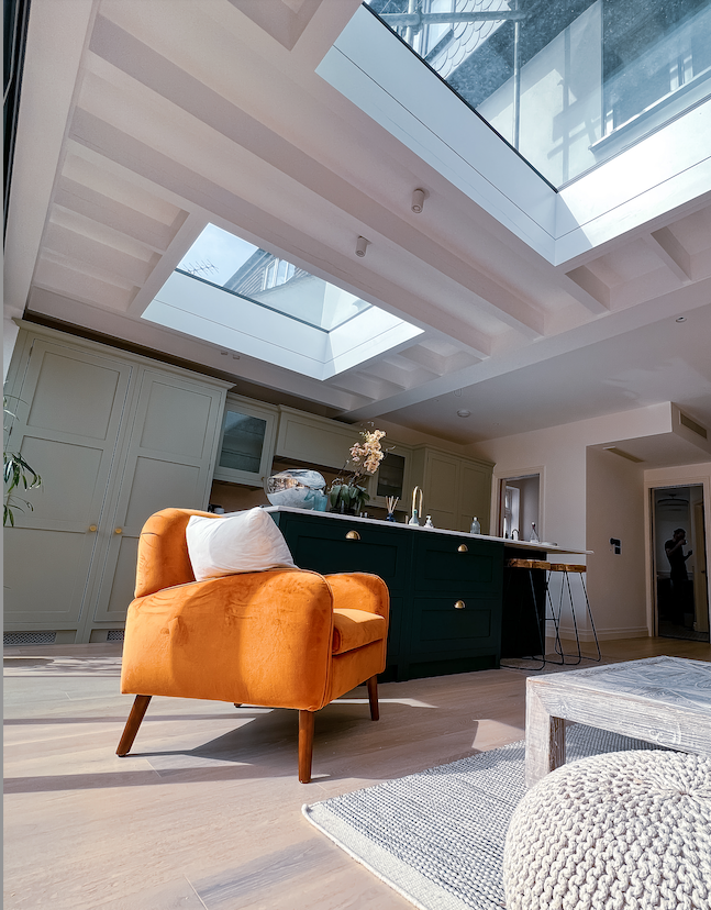 Orange armchair in bright room with skylight, dark green kitchen island, and light wood floors.