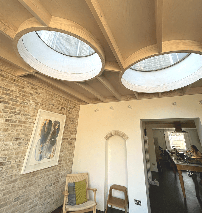 Interior with circular skylights, exposed beams, brick wall, artwork, and view into another room.