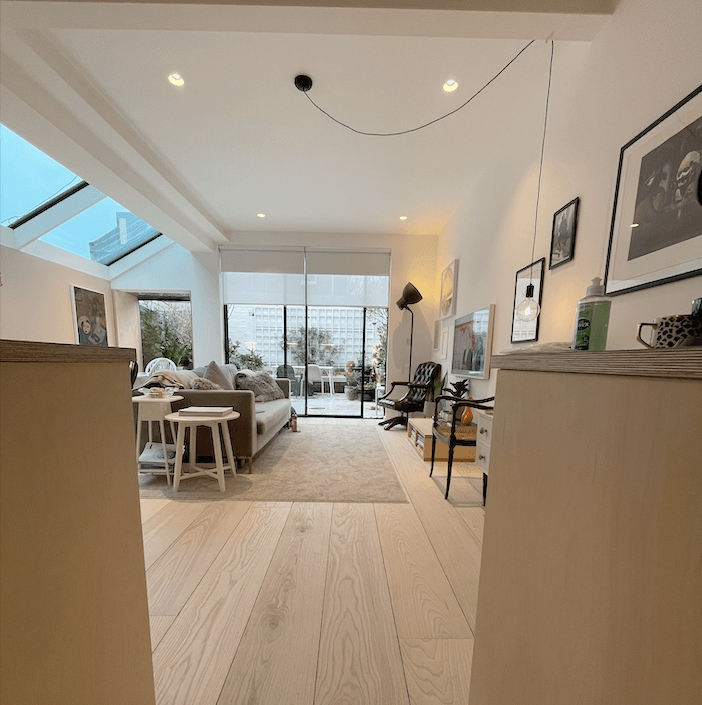 Bright living room with light wooden floors, sofa, rug, and large sliding doors to a patio.