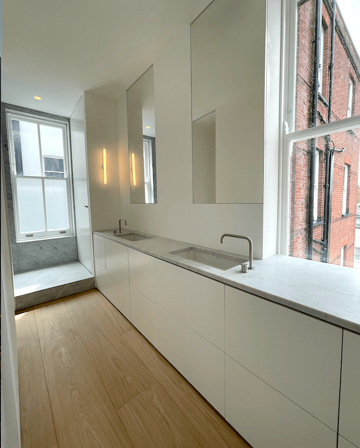 Modern white bathroom with two sinks, long counter, and tall windows.