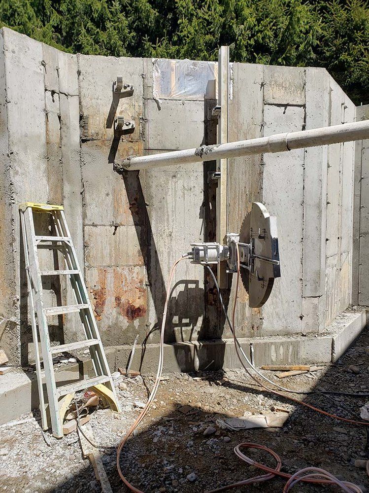 A ladder is sitting next to a machine that is cutting a hole in a concrete wall.