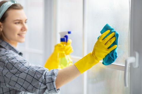 Housekeeper washing window glass with rag and spray detergent