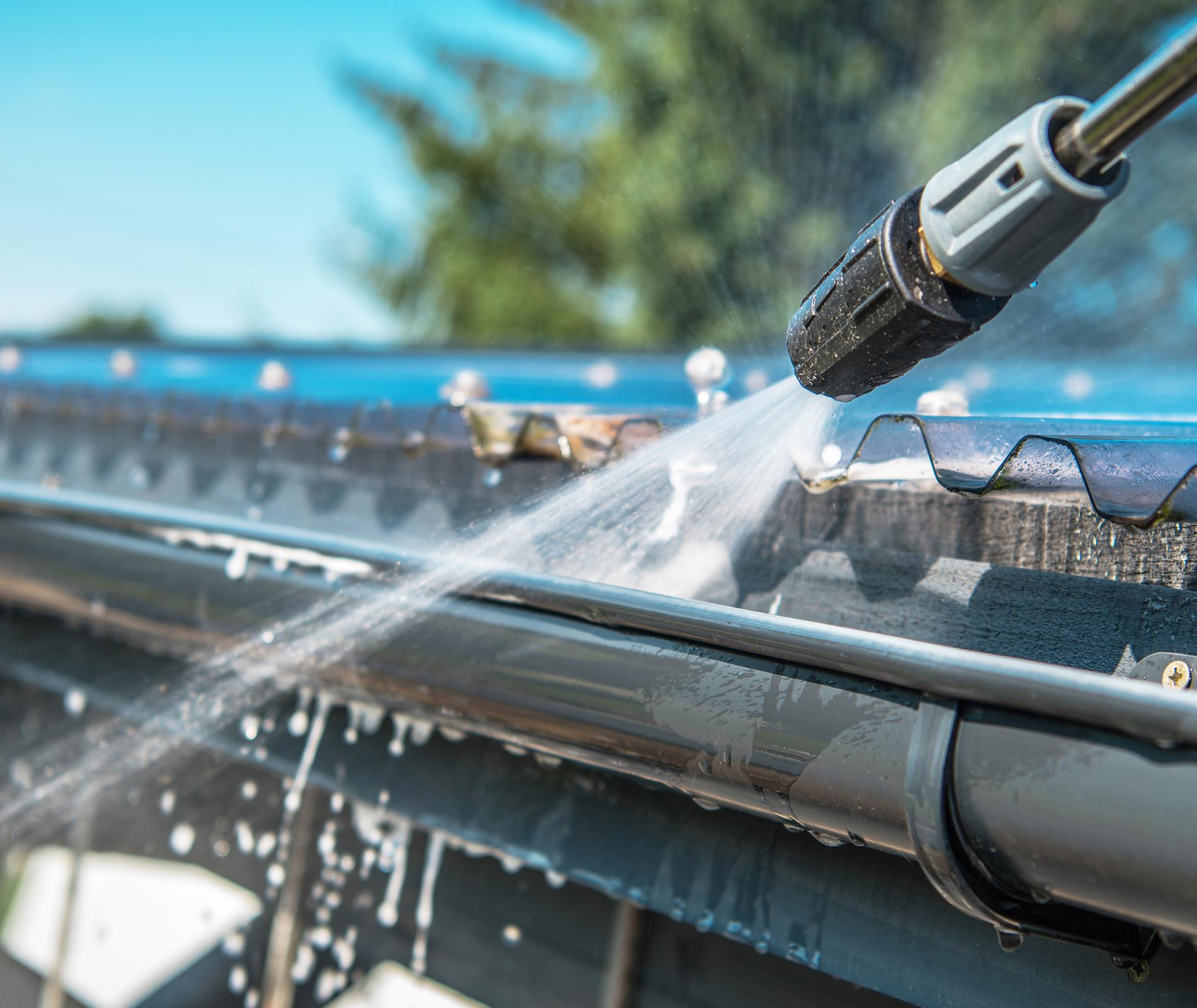 Power washing a rain gutter with a spray nozzle, water splashing in bright sunlight