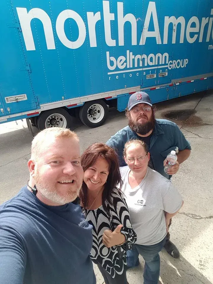 Four people smiling near a blue North American moving truck.