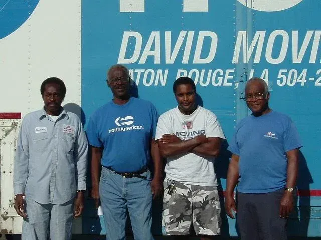 Four men standing in front of a blue moving truck. The truck has 