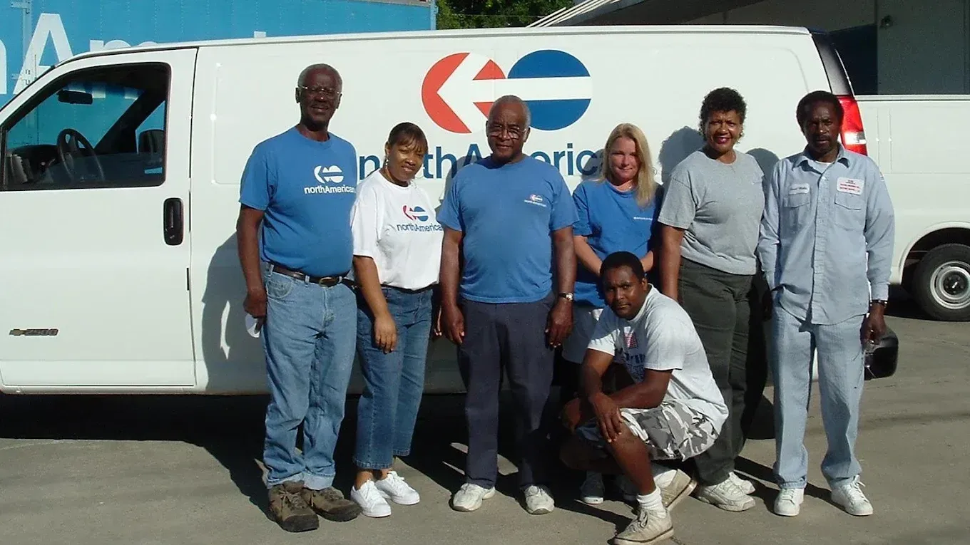 Group of people posing by a white van with a logo.