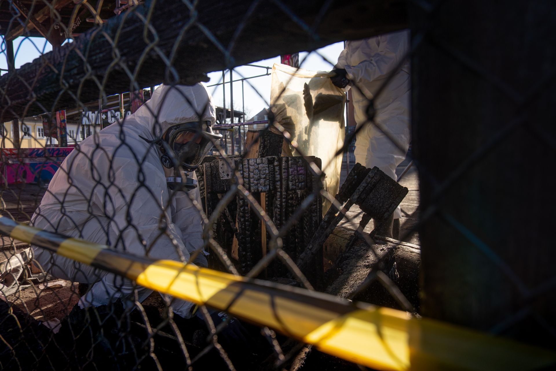 En mand i et hvidt jakkesæt står bag et trådhegn.