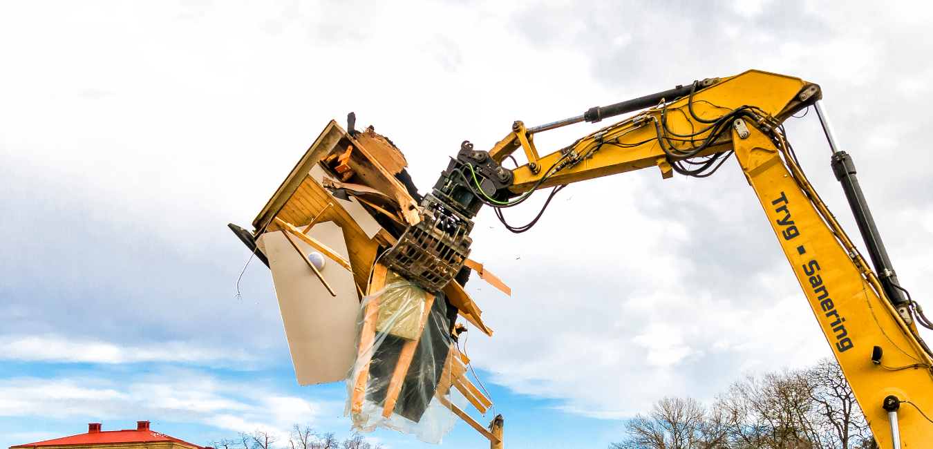 En gul gravemaskine er ved at nedrive et hus.