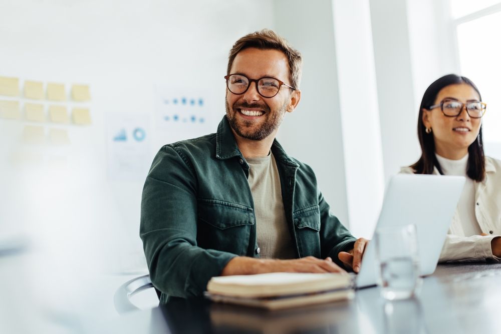 Two coworkers smiling at a table with a laptop in a bright  office — Compago Technologies In Cambridge, TAS