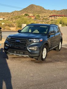 A black ford explorer is parked on a gravel road in front of a mountain.
