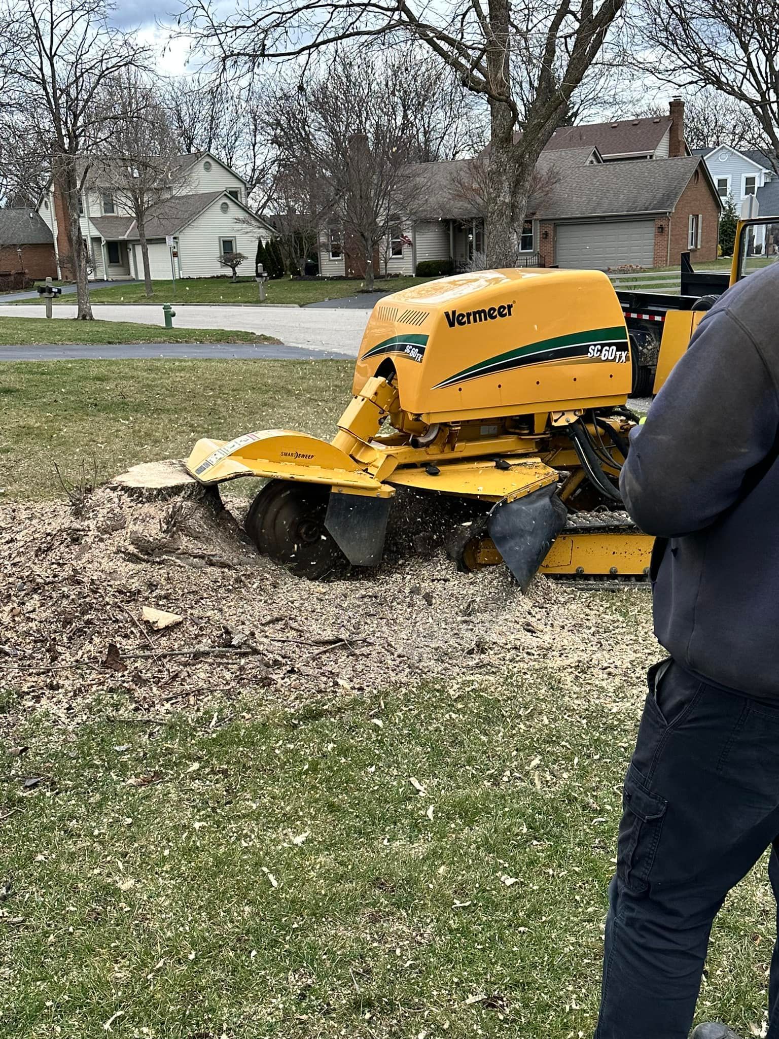 A man is standing next to a stump grinder in a yard.