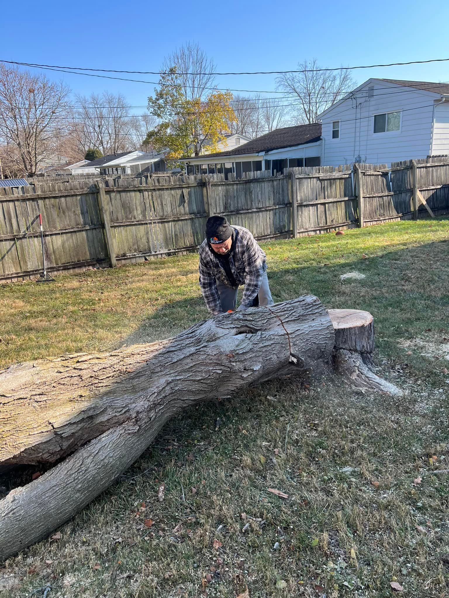 A man is cutting a tree stump with a chainsaw.