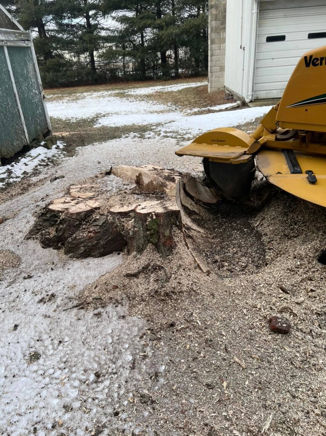 A stump grinder is grinding a tree stump in a driveway.