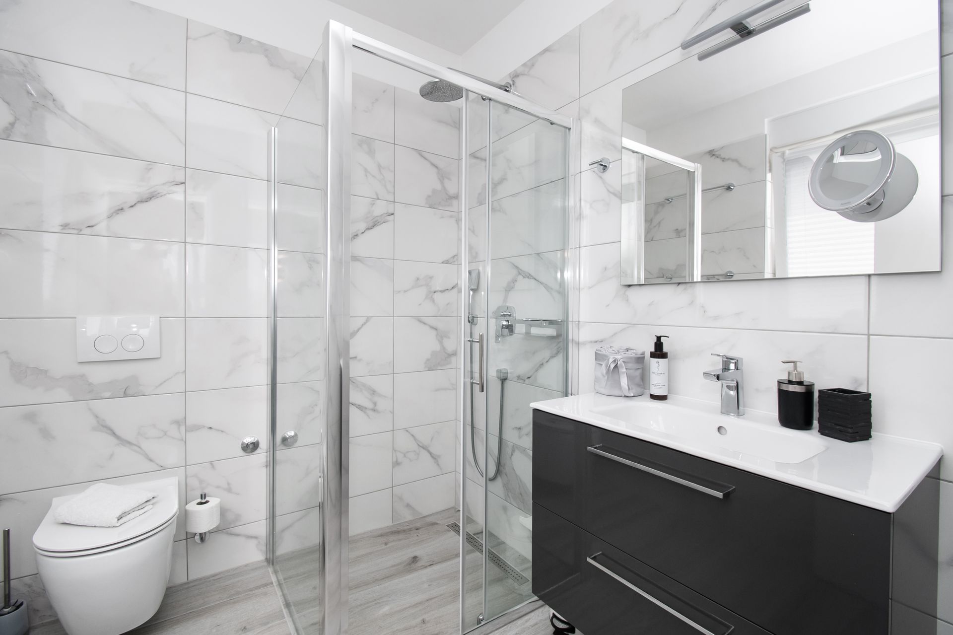 Modern bathroom with white marble tiles, glass shower, and dark gray vanity.