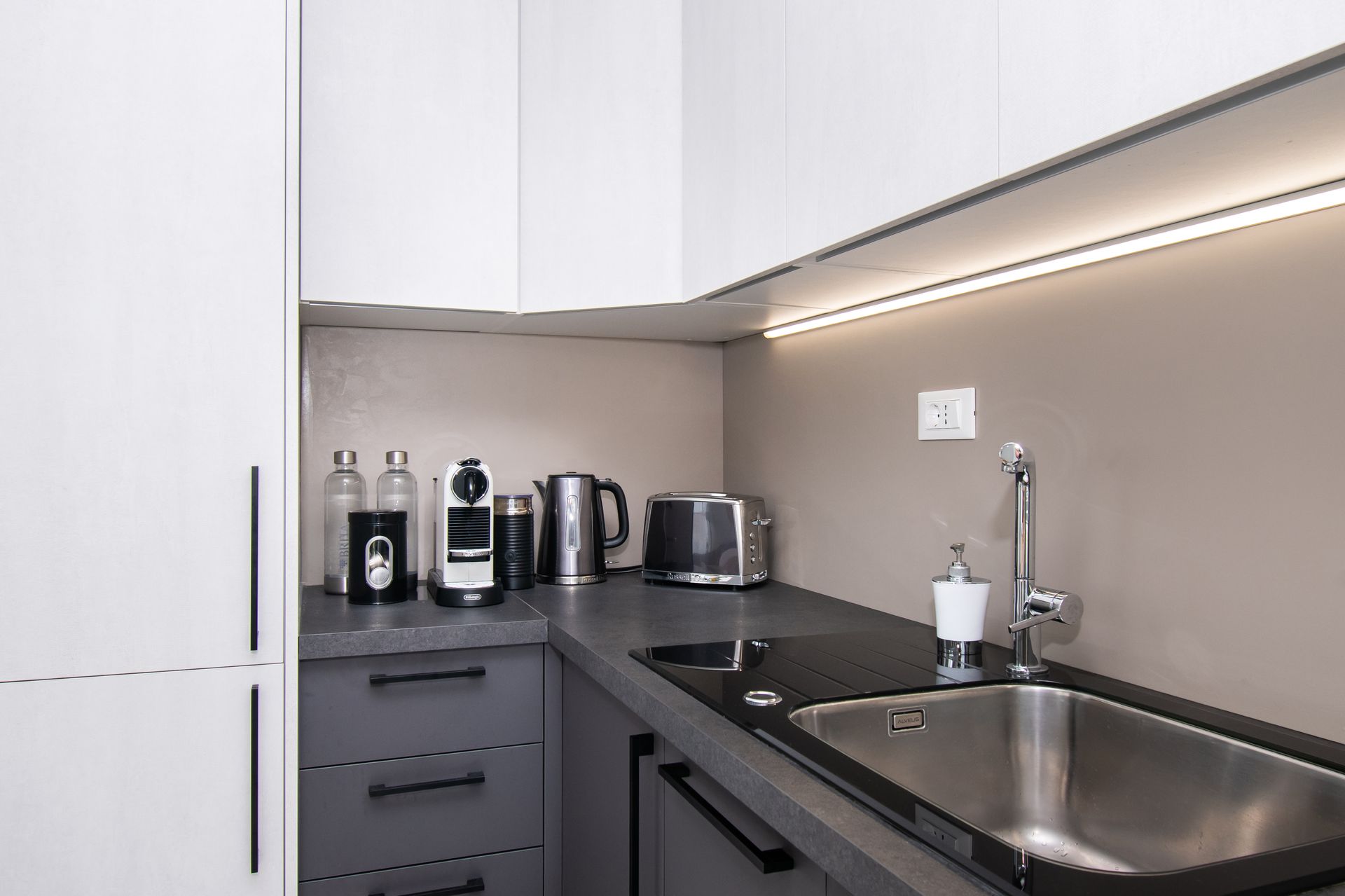 Modern kitchen with gray cabinets, sink, appliances, and countertop lighting.