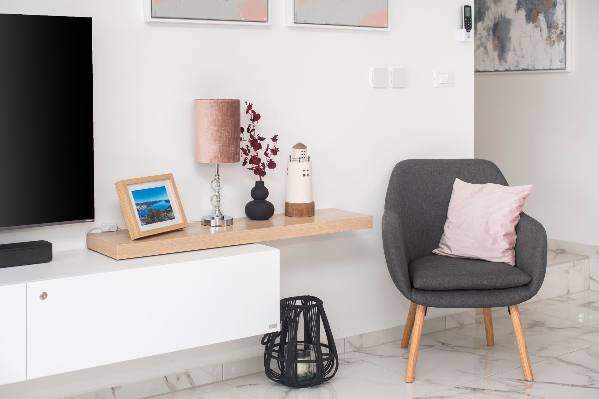 Living room with white wall, TV, floating shelf, gray chair, and decor.