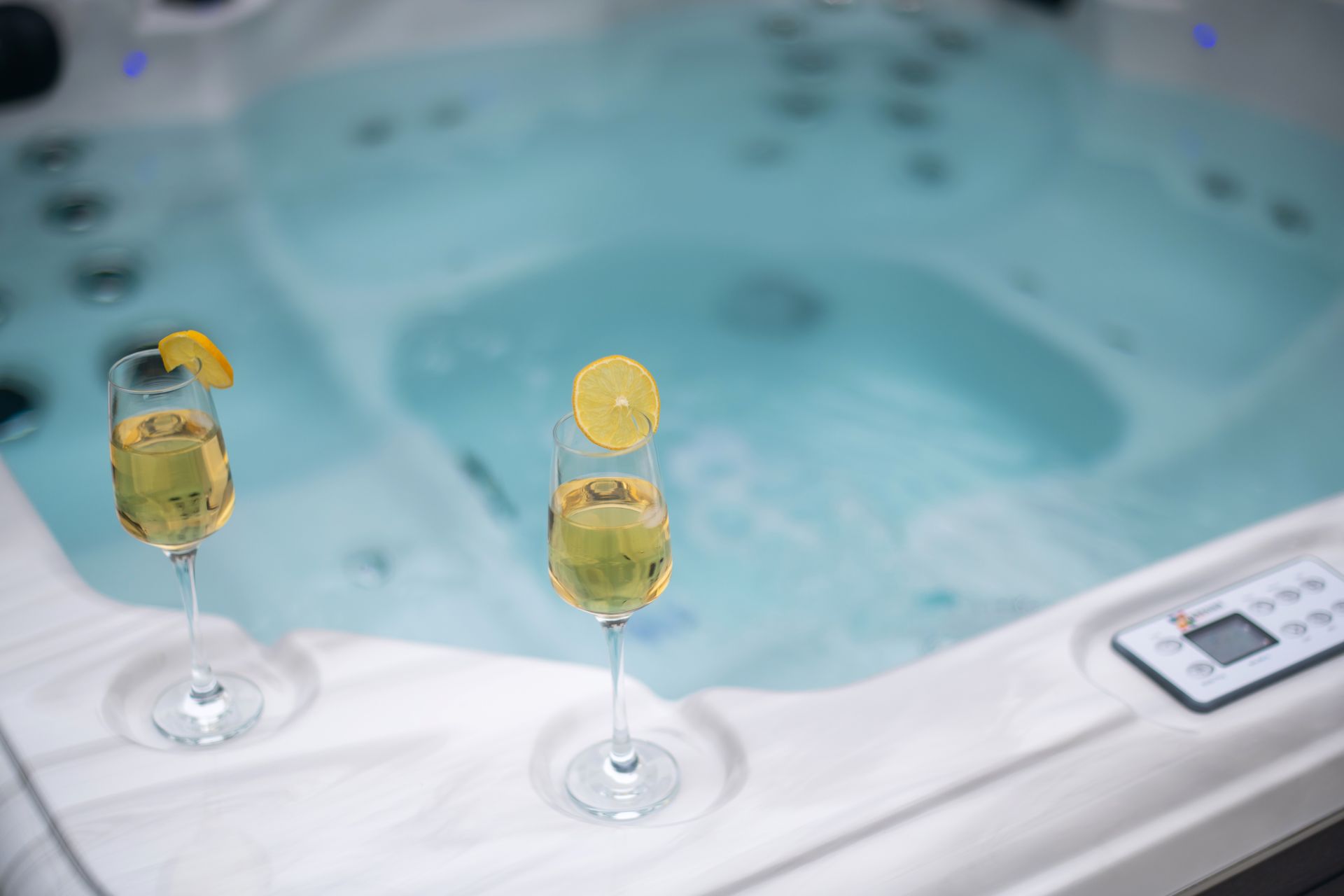 Two champagne flutes with lemon slices sit on the edge of a hot tub.
